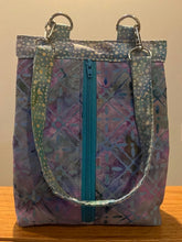 Load image into Gallery viewer, Multicolored patterned bag with a blue zipper on a wooden surface.