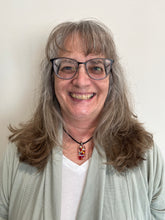 Load image into Gallery viewer, Person with gray hair and glasses smiling against a plain background
