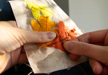 Load image into Gallery viewer, Person stitching fabric with orange and yellow leaves on a white background
