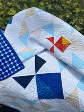 Load image into Gallery viewer, Quilt with geometric patterns in blue, red, and yellow on a green outdoor background
