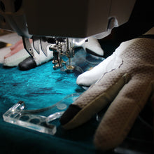 Load image into Gallery viewer, Close-up of a sewing machine with a gloved hand guiding fabric
