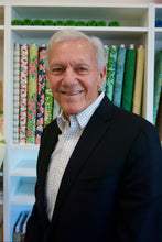 Load image into Gallery viewer, Man standing in front of a shelf with colorful fabric rolls
