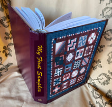 Load image into Gallery viewer, Open book titled 'My First Sampler' with quilt pattern design on cover
