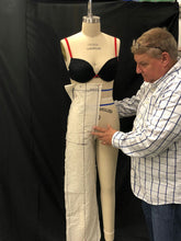 Load image into Gallery viewer, Man adjusting a mannequin wearing a black bra and white pants against a black background
