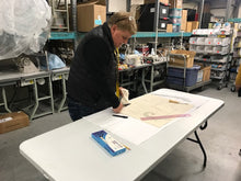 Load image into Gallery viewer, man standing over a table cutting fabric
