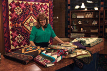 Load image into Gallery viewer, Nancy standing behind a table with a selection of quilts
